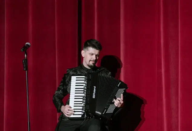 Aleksei Chebeliuk performing accordion in front of red curtains